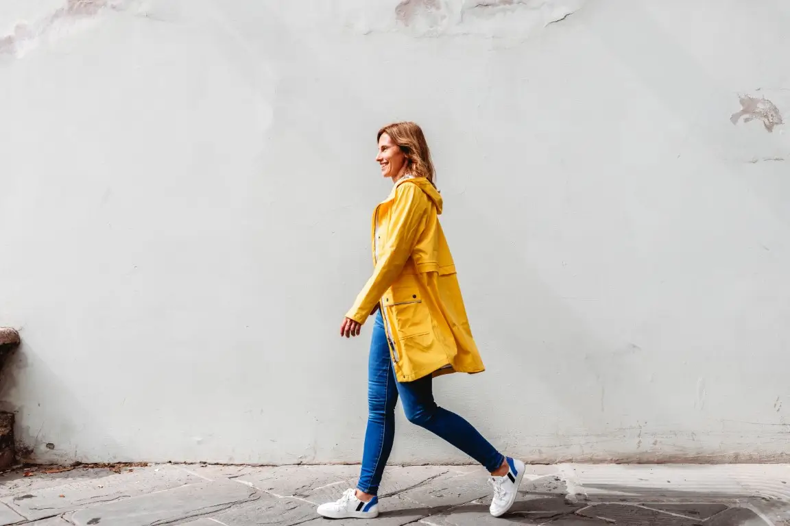 happy woman walking on a street in a city in front of a wall.