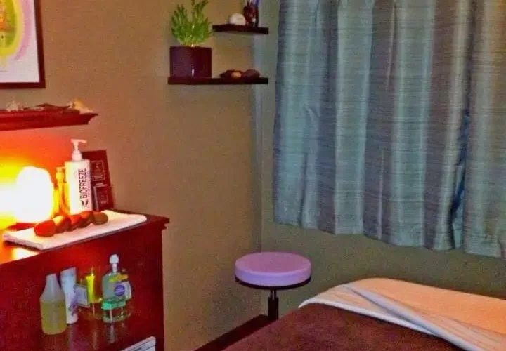 A massage room featuring a massage bed, a desk, and shelves filled with various wellness products.